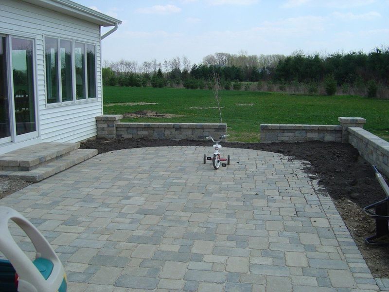 Brick patio with retaining walls, a tricycle, and a grassy backyard.