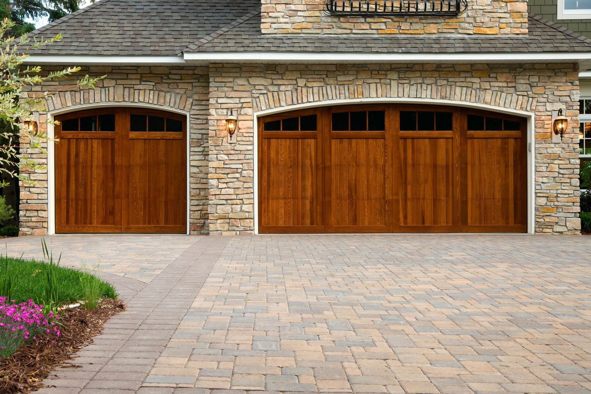 Two wooden garage doors with stone accents and paved driveway.