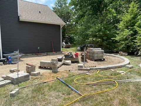 Construction of a circular patio near a house, with bricks and tools in a grassy yard.