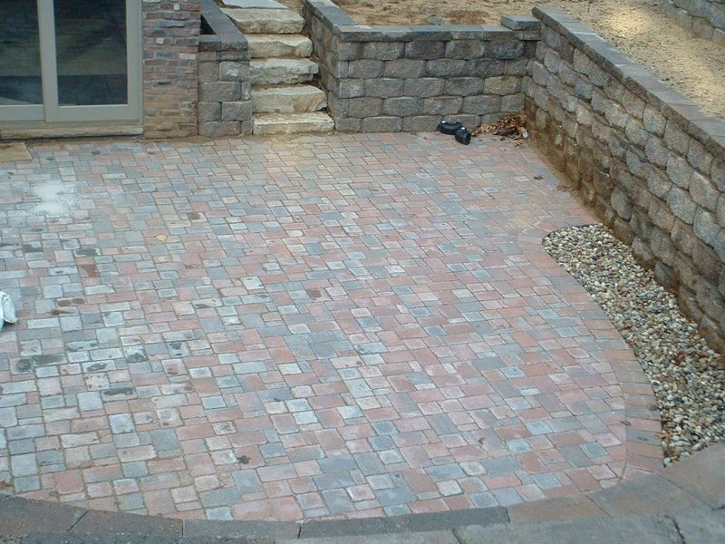 Brick patio surrounded by stone retaining walls and steps leading up.