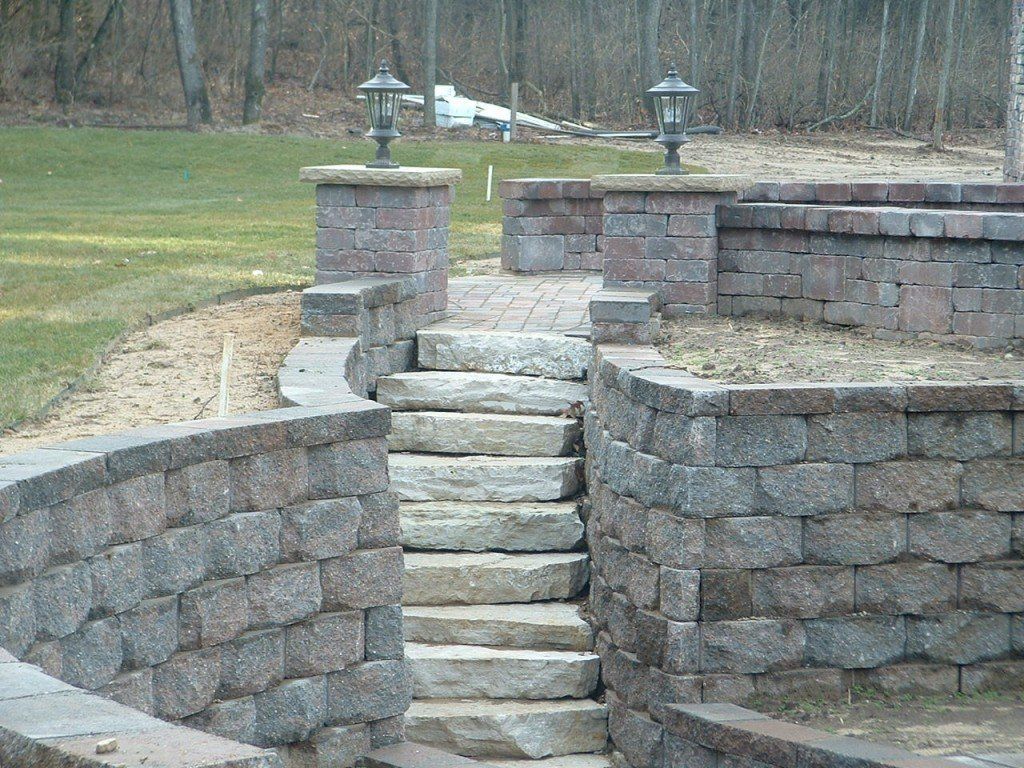 Stone steps between brick retaining walls, leading to a grassy area with two lamps.