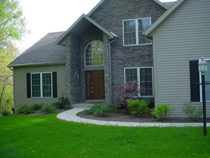 House with stone facade and beige siding, arched entryway, and landscaped front yard with green lawn.