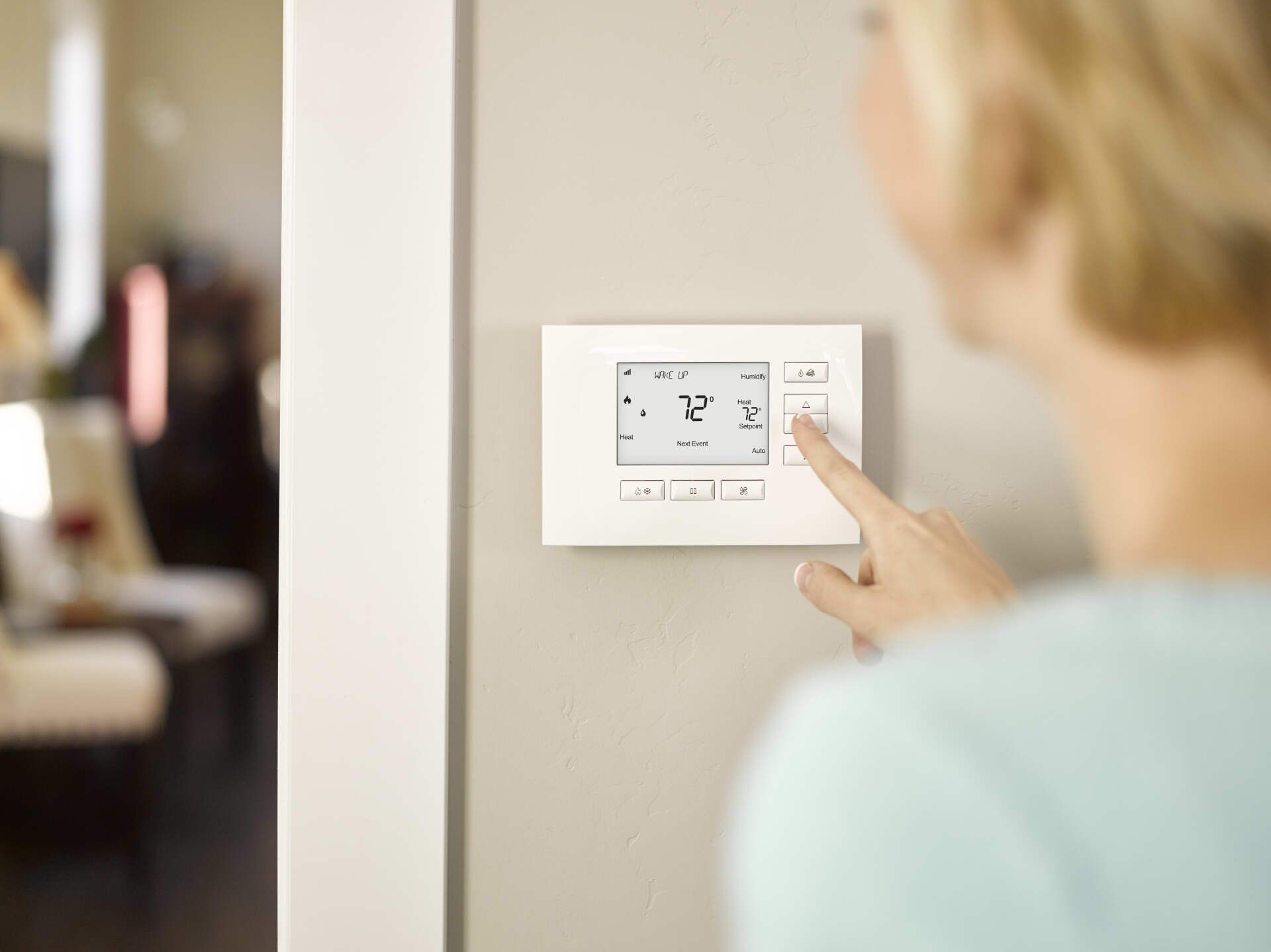 A woman is pressing a button on a thermostat.