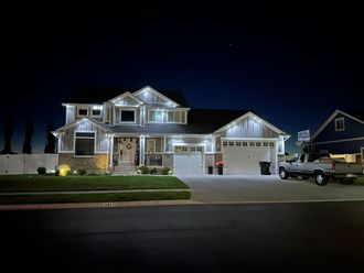 A large house is lit up at night with a truck parked in front of it.