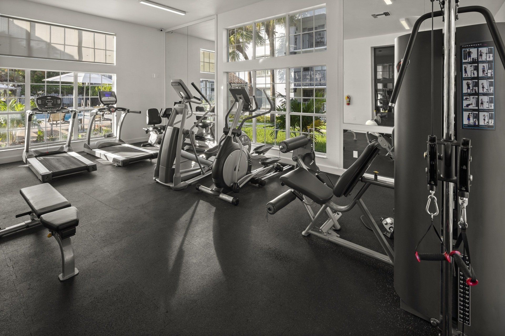 Gym interior with treadmills, elliptical, weight machines, and natural light.