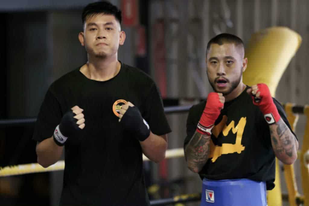 Two boxers in a gym; one with black gloves, the other with red hand wraps. They face the camera.