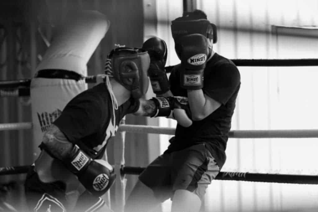 Two boxers sparring in a ring, wearing headgear and gloves, one throwing a punch.