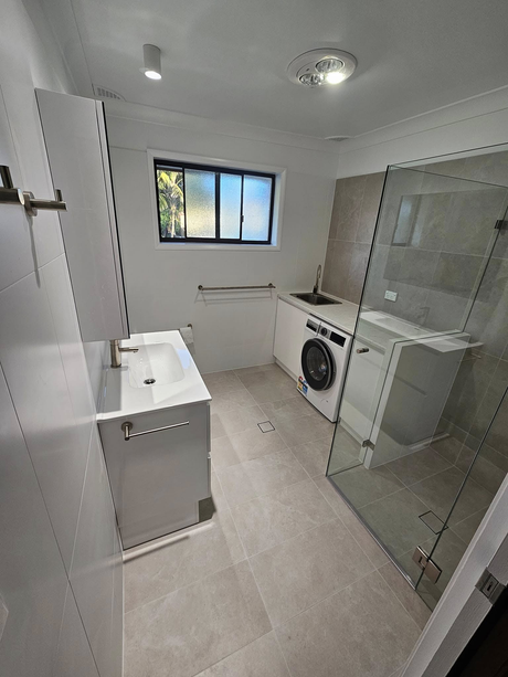 A bathroom with a sink , washing machine , and shower.