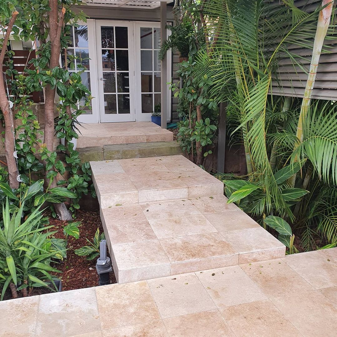 A walkway leading to a house with french doors surrounded by trees and plants.