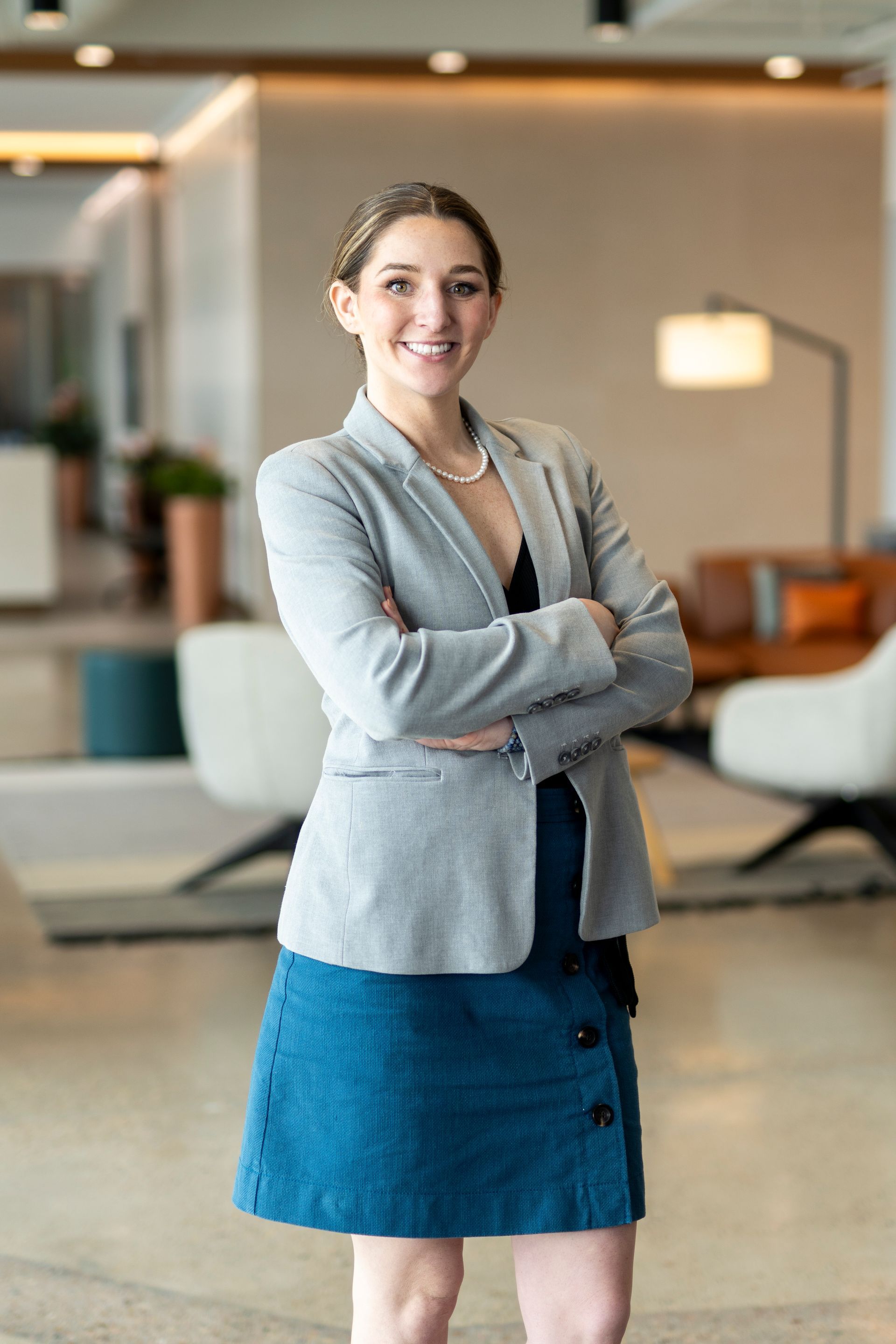 A woman in a suit is standing with her arms crossed and smiling.