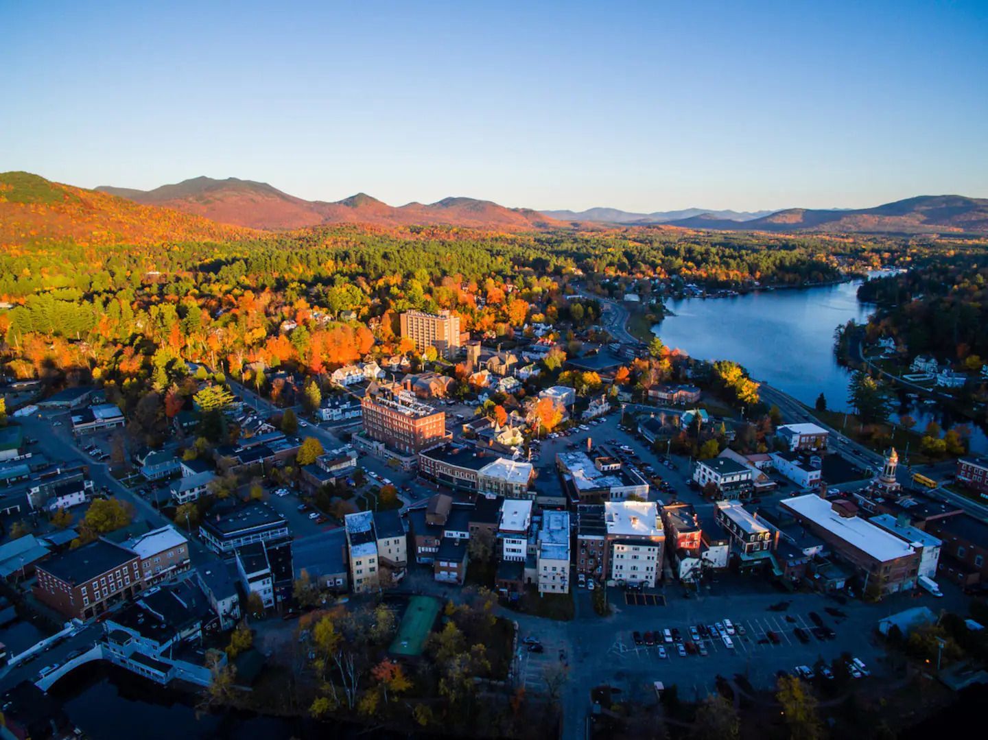 An aerial view of a small town with a lake and mountains in the background.