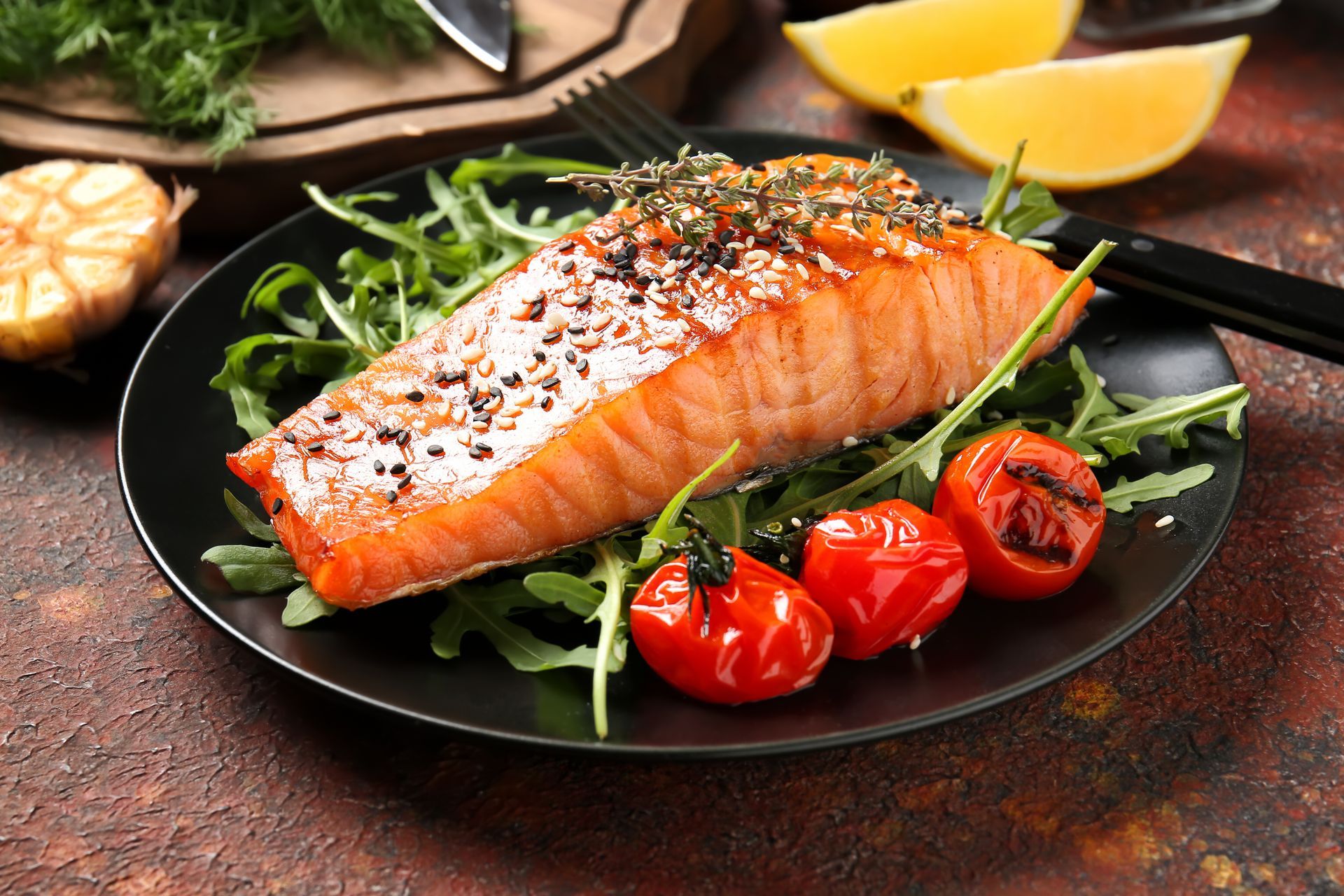 A black plate topped with a piece of salmon and tomatoes.