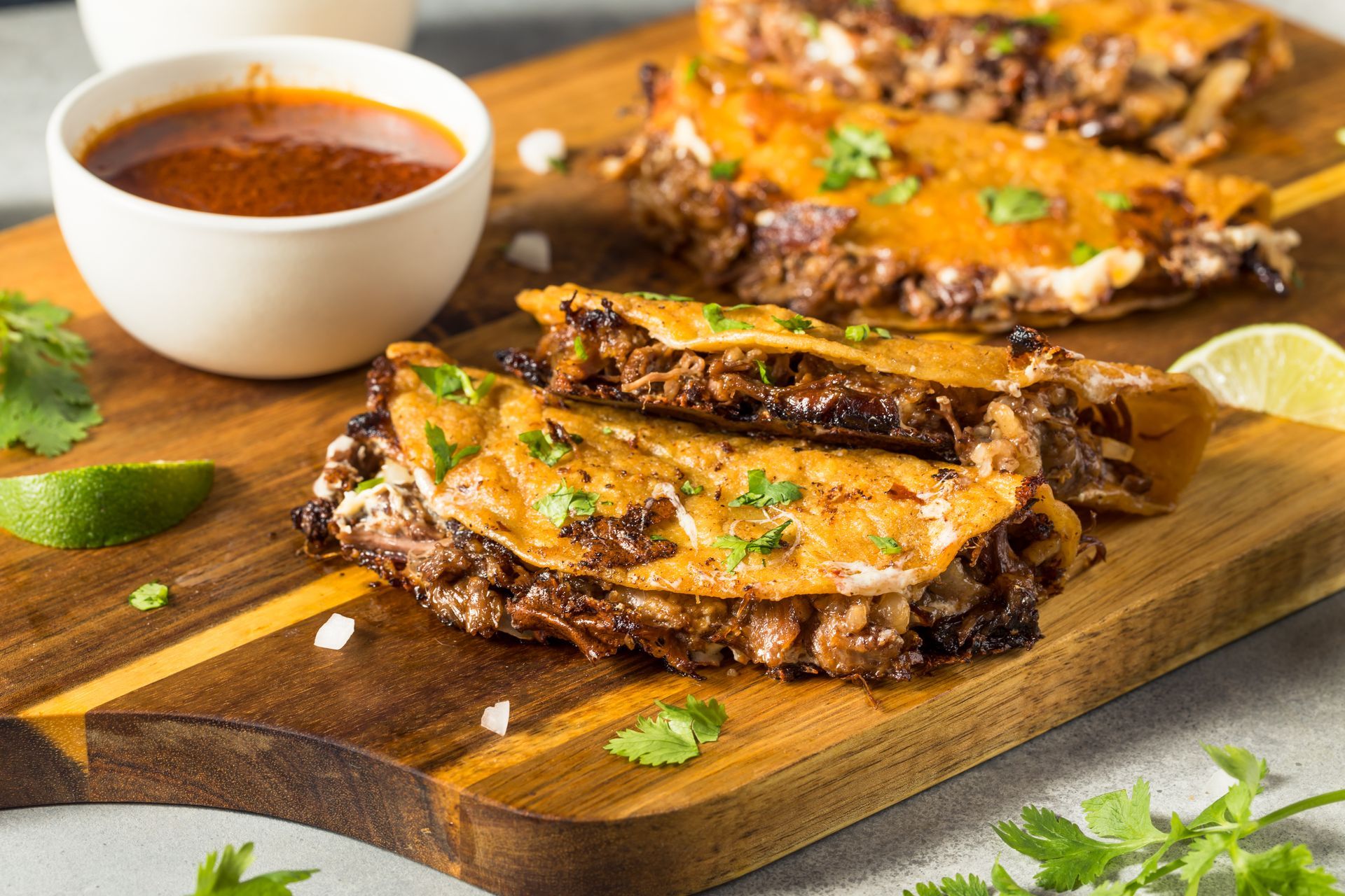 A wooden cutting board topped with tacos and a bowl of sauce.
