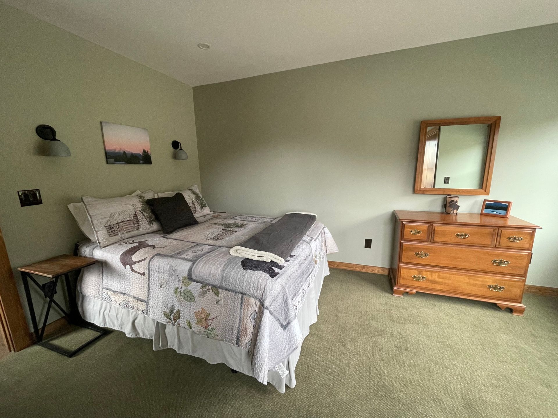A bedroom with a bed , dresser , mirror and nightstand.