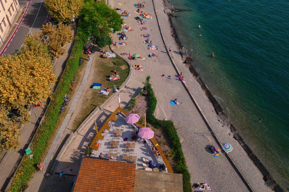 Due uomini a torso nudo brindano su una spiaggia, sotto un cartello a forma di cuore che dice 