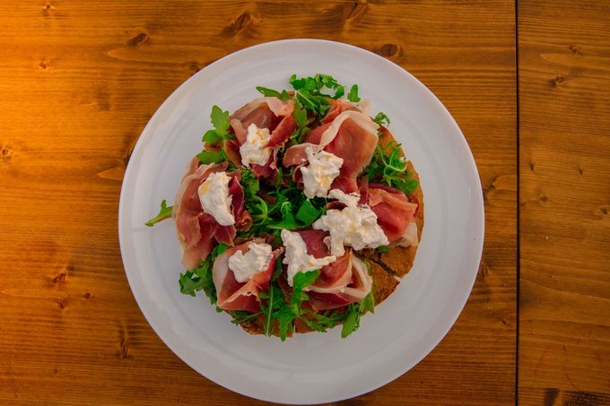 Focaccia con prosciutto, rucola e ricotta su un piatto bianco.