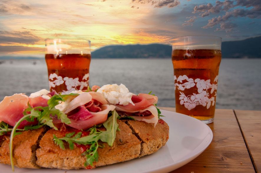 Panino con prosciutto, birra e tramonto sull'acqua.