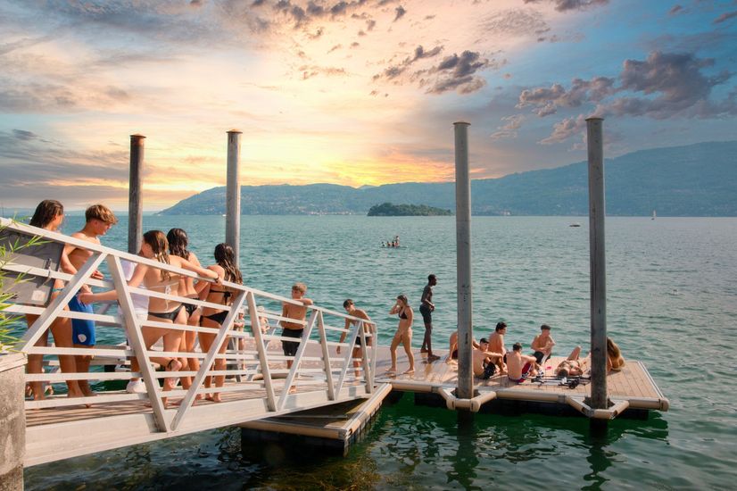 Persone su un molo sull'acqua al tramonto. Montagne e isole sullo sfondo.