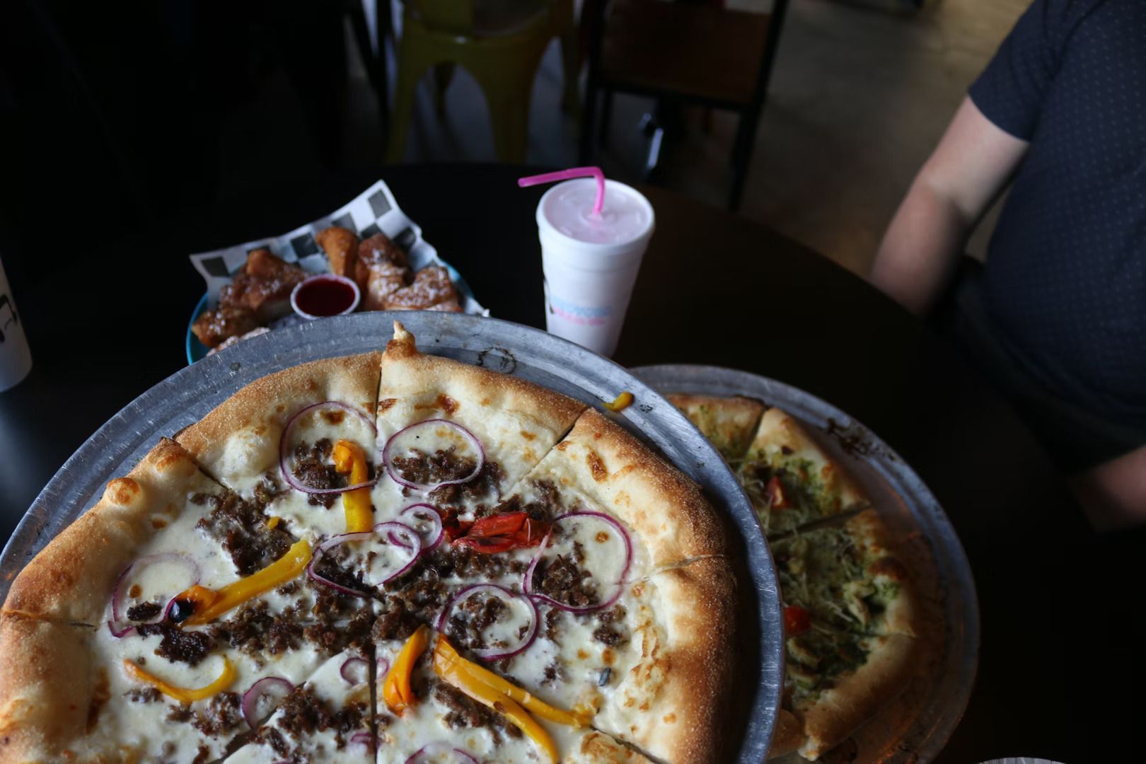 Two pizzas are sitting on a table next to a drink.