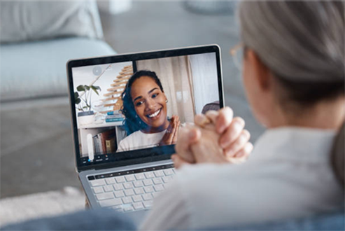 A woman is sitting in front of a laptop computer talking to another woman.