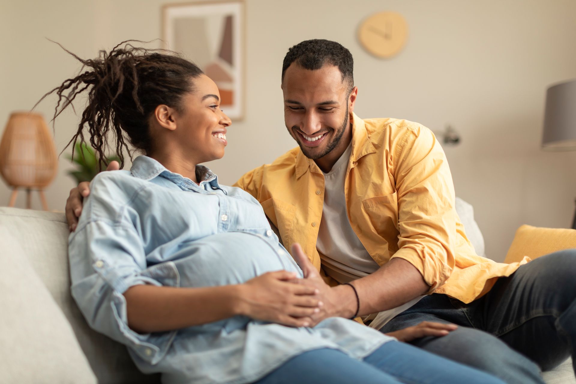 A pregnant woman is sitting on a couch with her husband.