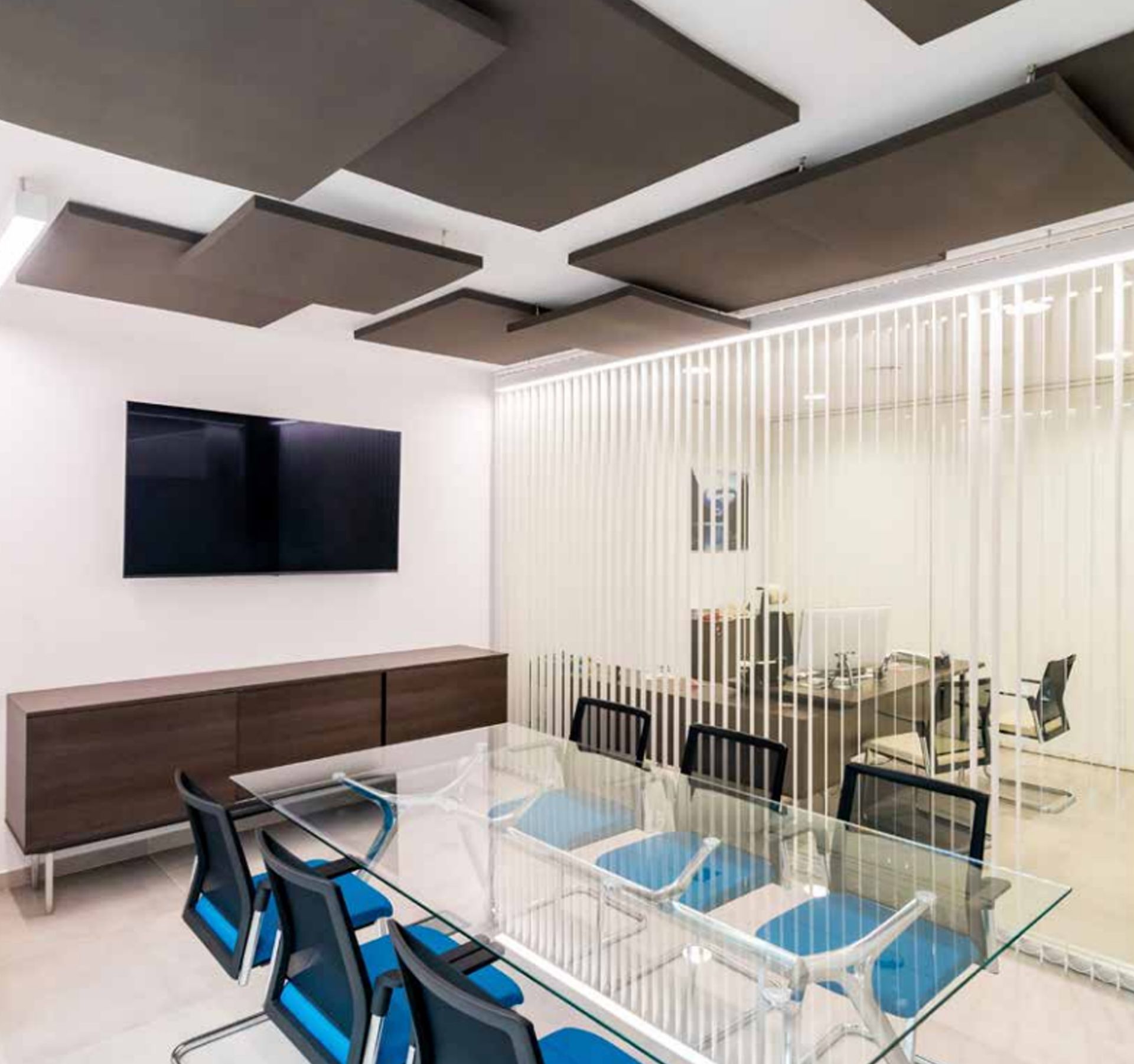 Una sala de conferencias con una mesa y sillas de cristal y un televisor de pantalla plana en la pared.