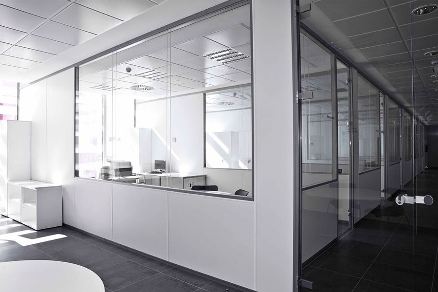 Un largo pasillo con paredes blancas y mamparas de cristal en una oficina.