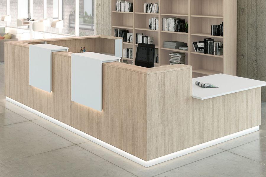 Un largo mostrador de recepción de madera en una oficina con una estantería detrás.