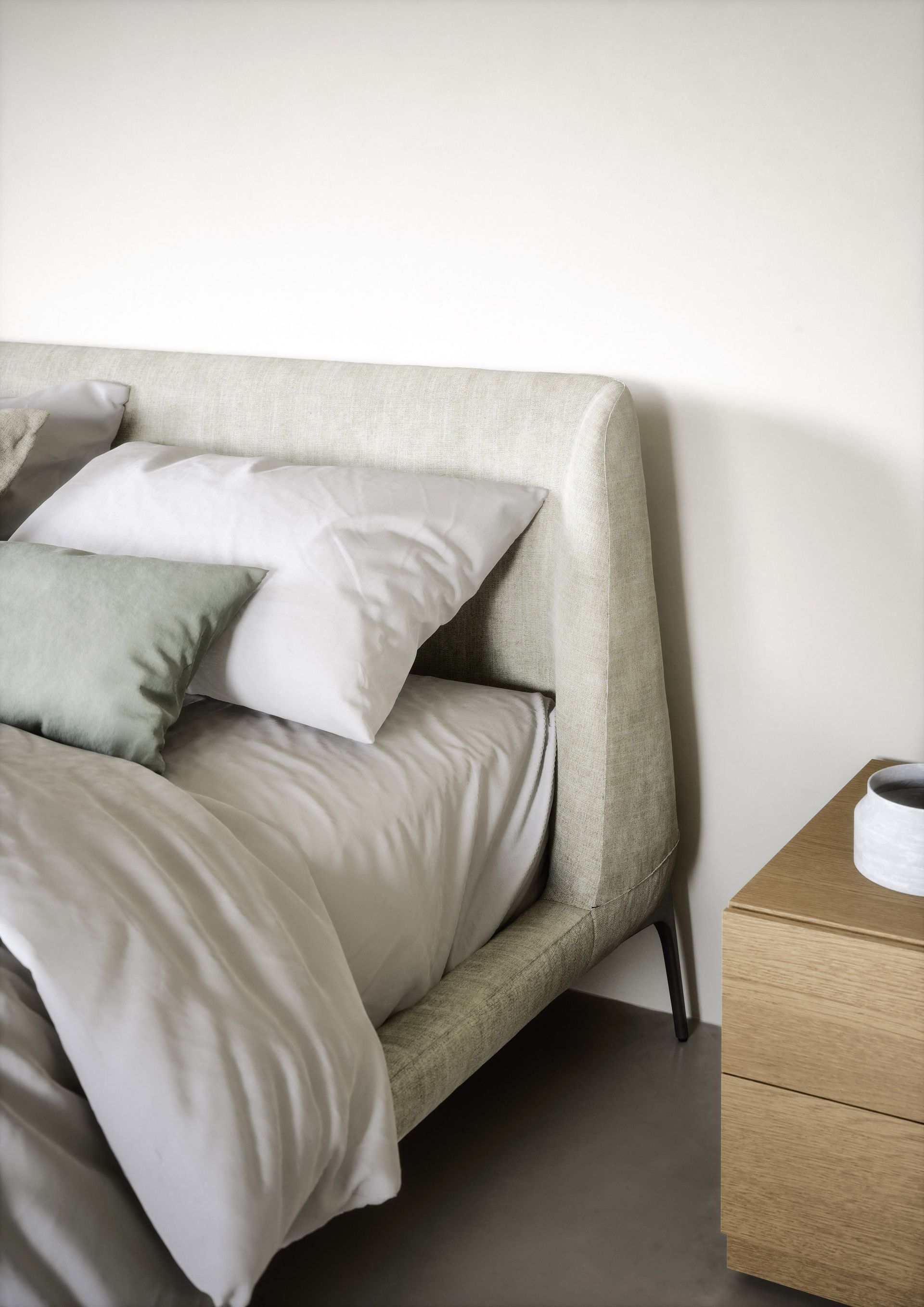 Una cama con sábanas blancas y almohadas al lado de una mesa de noche