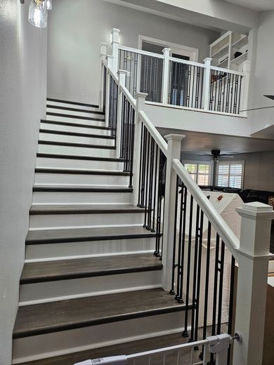Staircase with white risers and dark treads, black wrought iron railing, leading to a second-floor balcony.