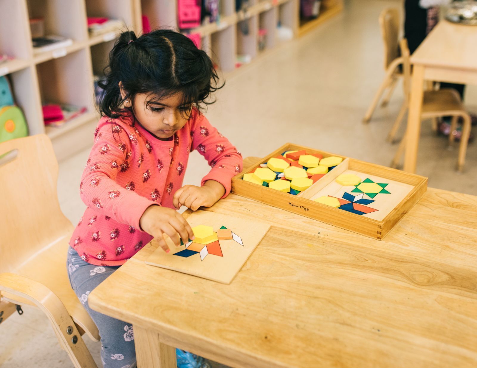 A little girl is sitting at a table playing with a puzzle.