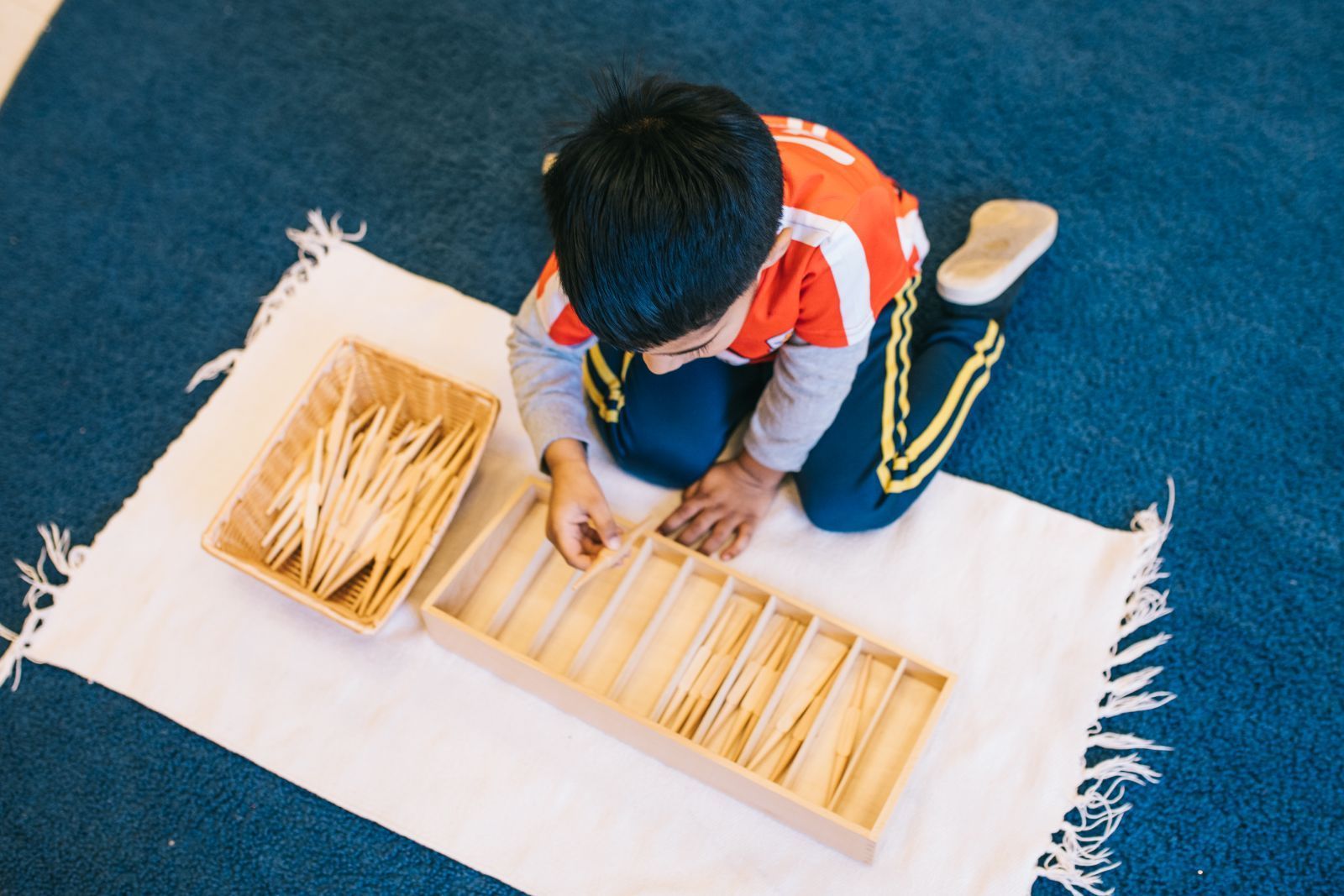 A young boy is kneeling on the floor playing with wooden sticks.