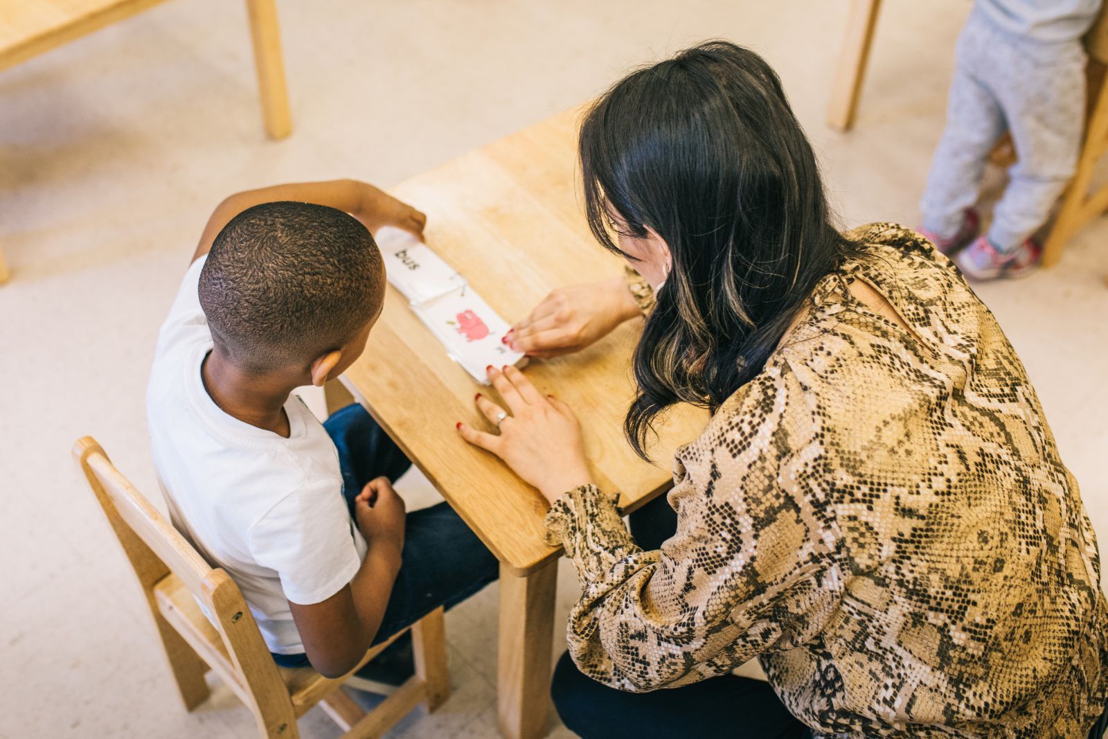 A woman is kneeling down next to a child sitting at a table.