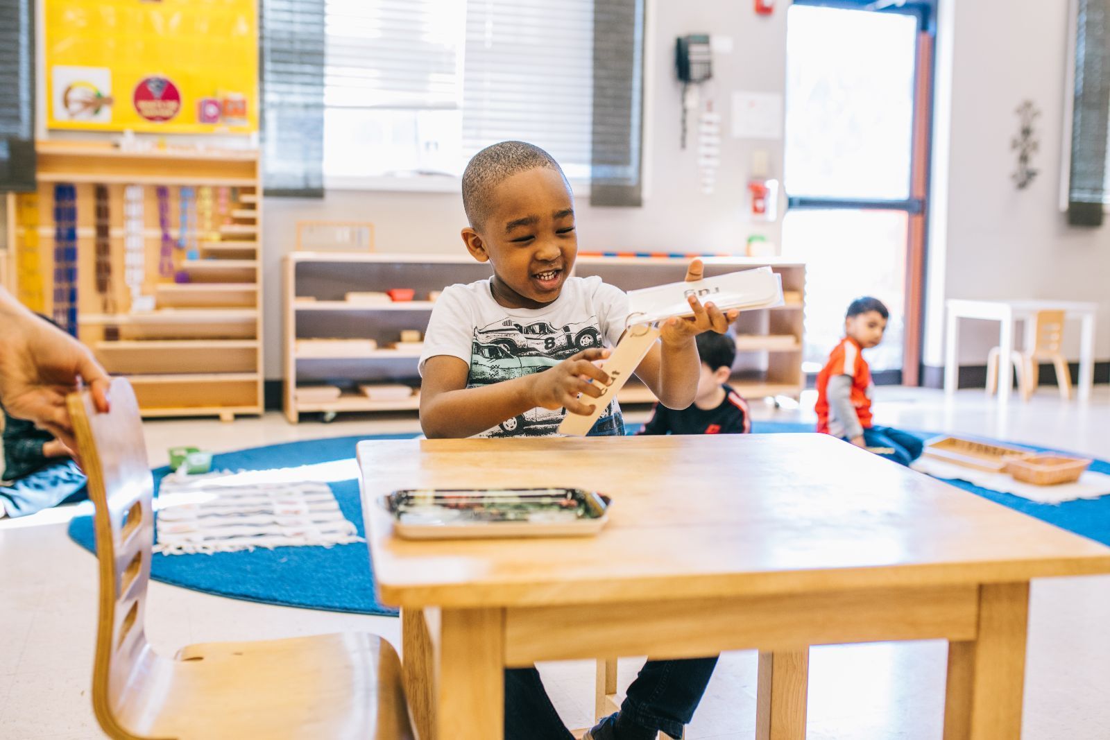A young boy is sitting at a table in a classroom holding a piece of wood.