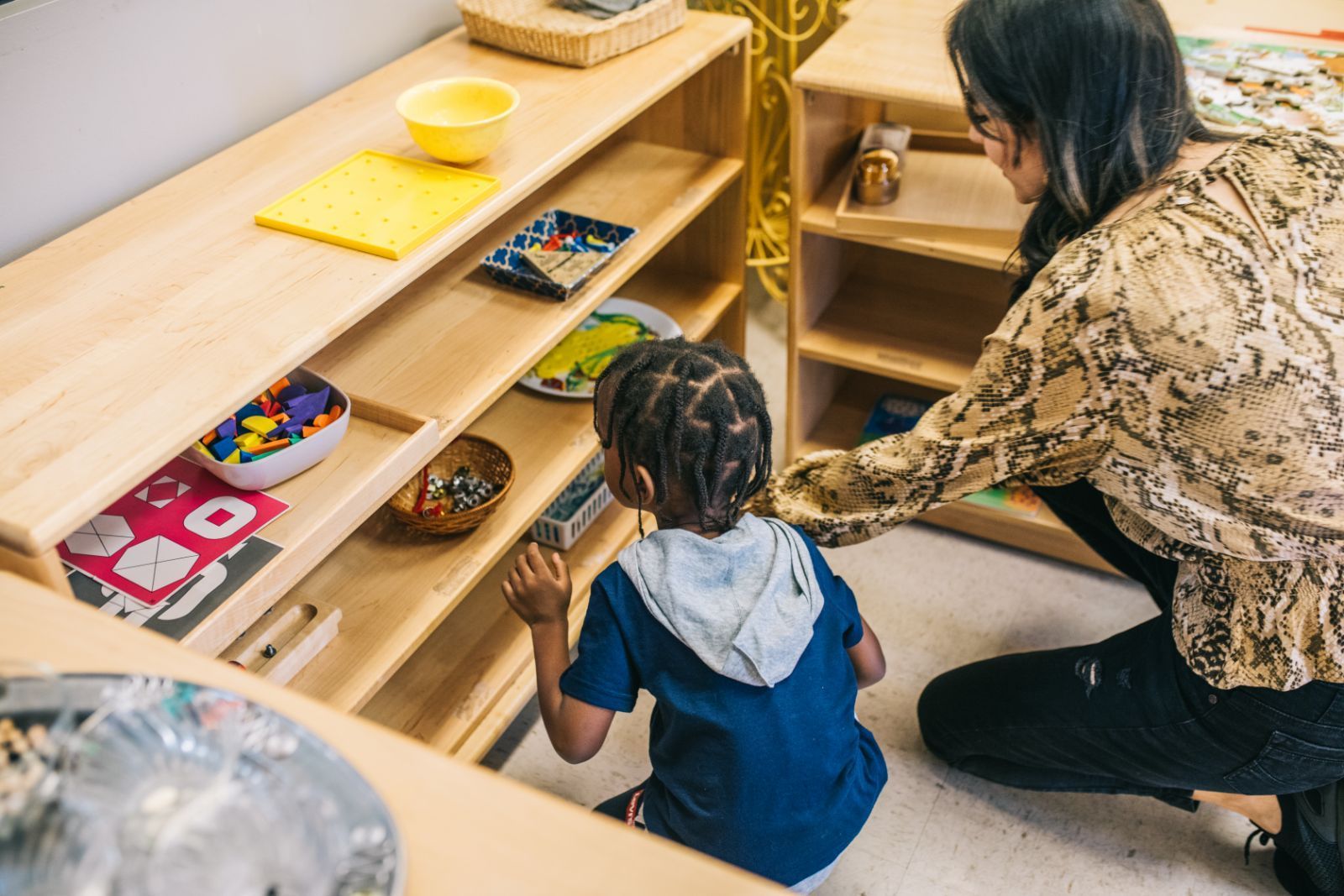 A woman is kneeling down next to a child looking at a shelf.