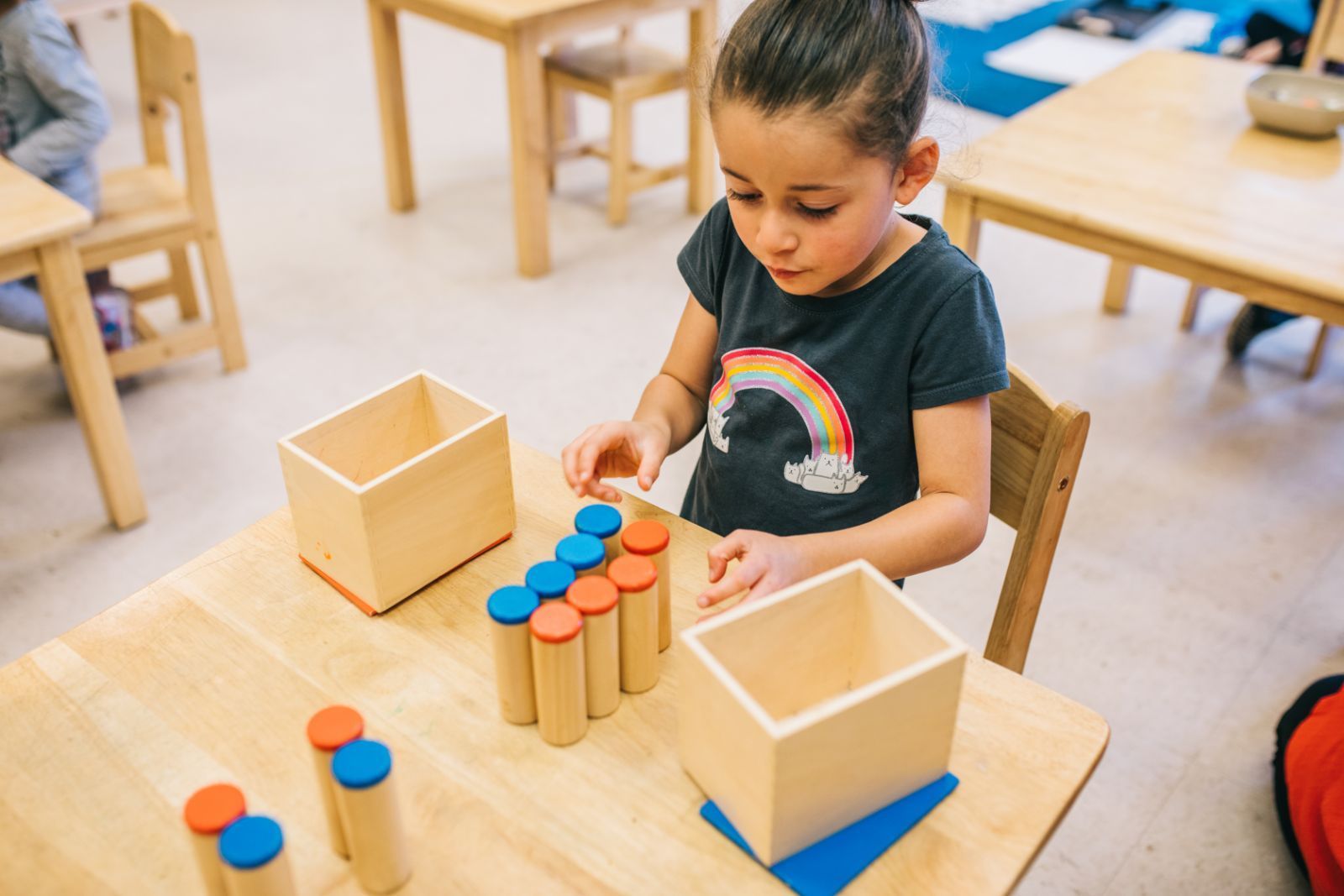 A little girl is sitting at a table playing with wooden toys.