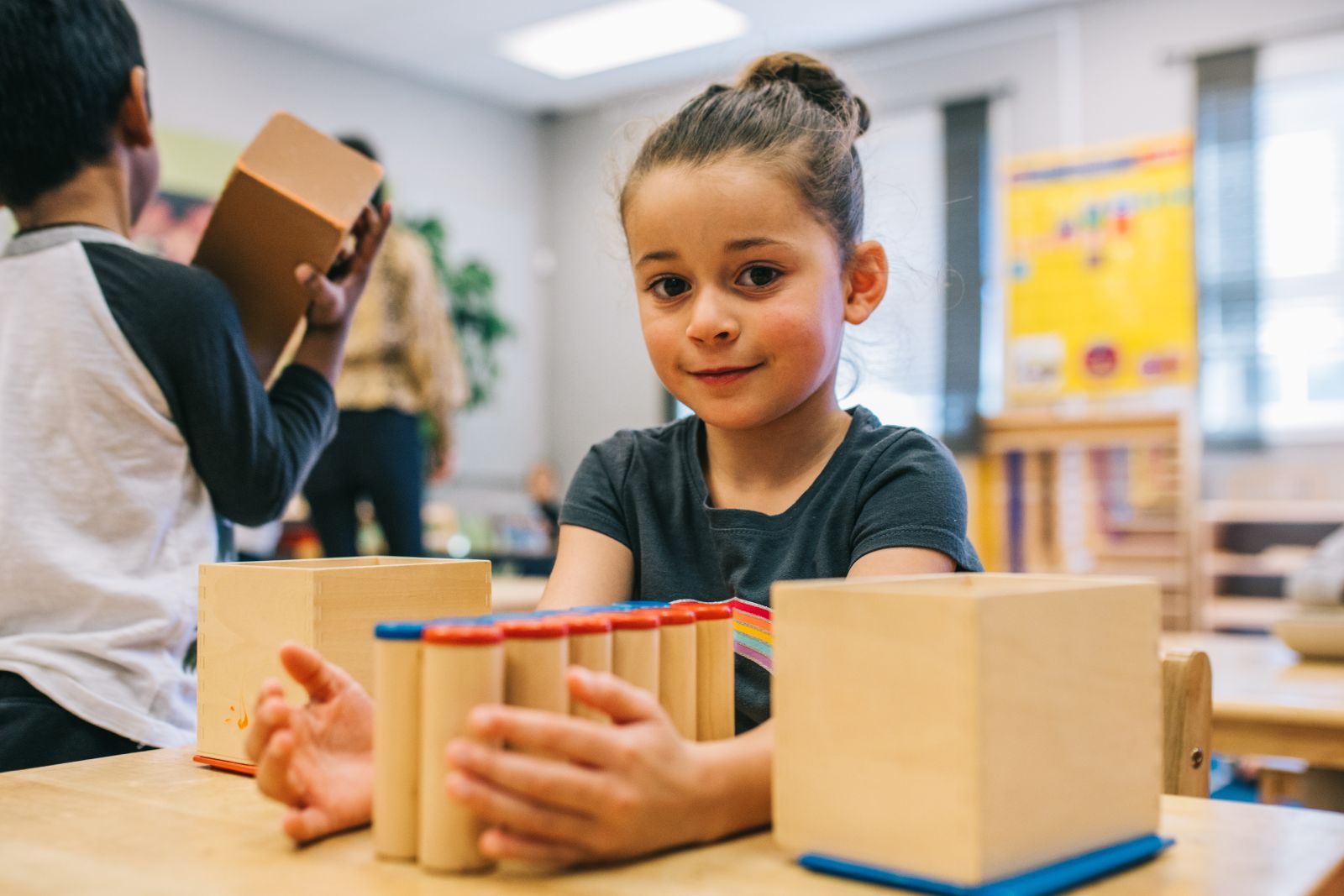 A little girl is sitting at a table playing with wooden blocks.
