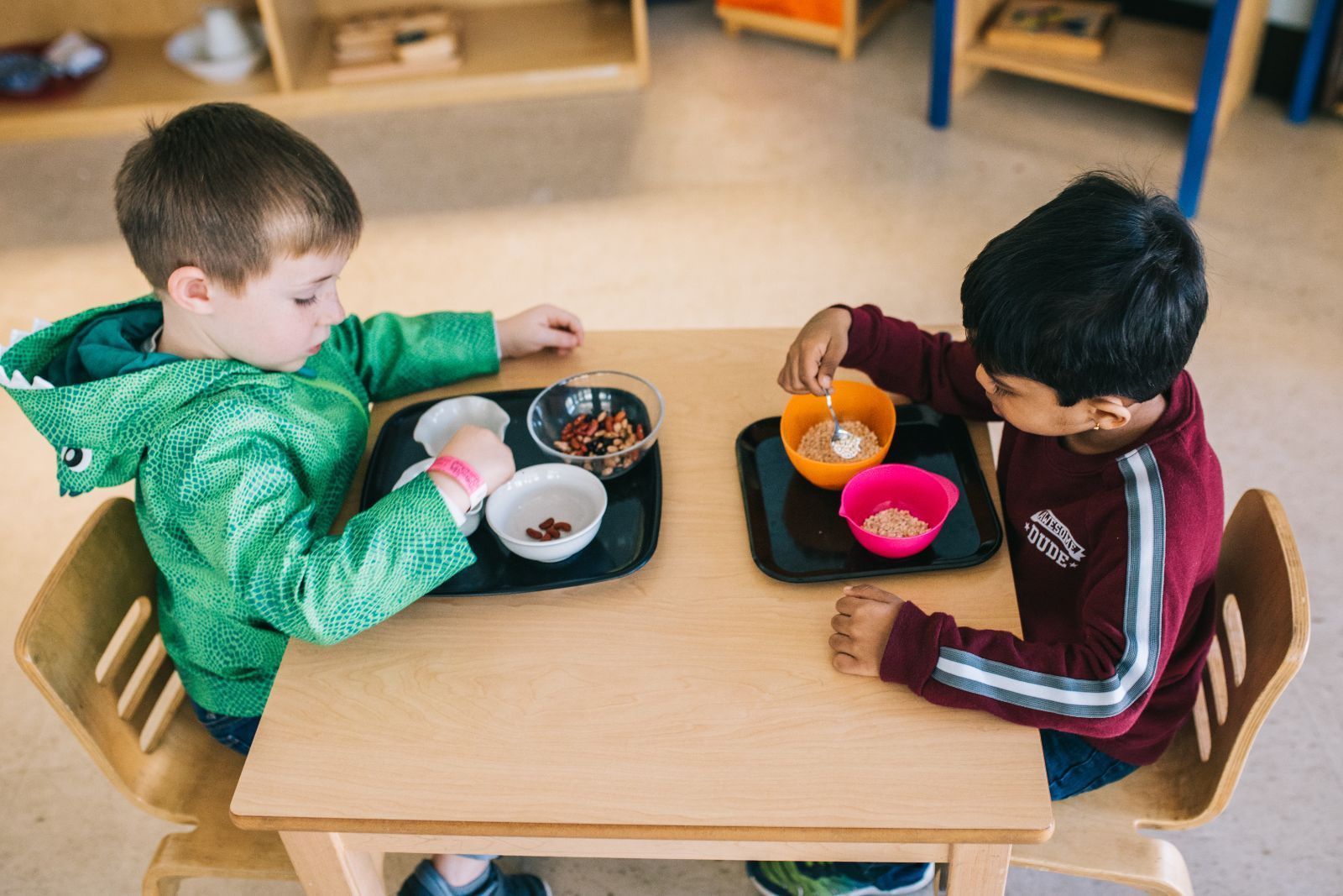 Two young boys are sitting at a table with bowls of food.