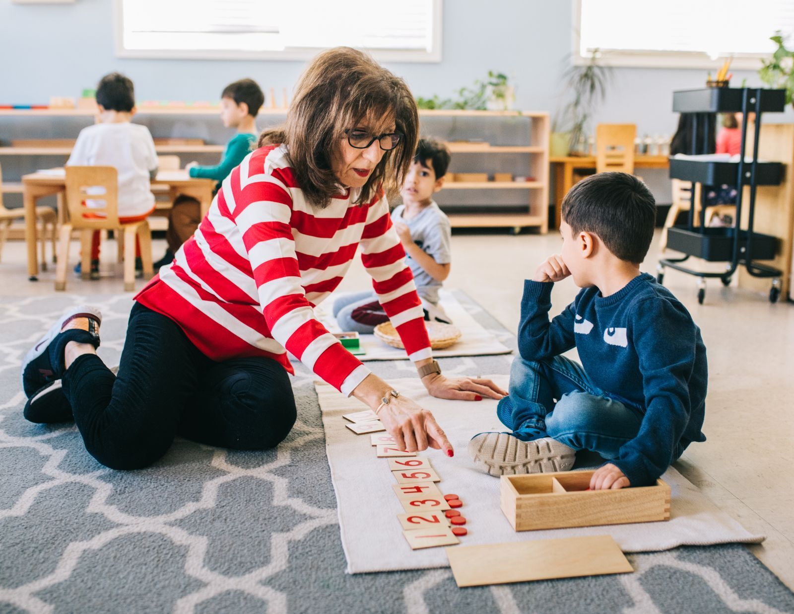A woman is kneeling on the floor playing with children in a classroom.