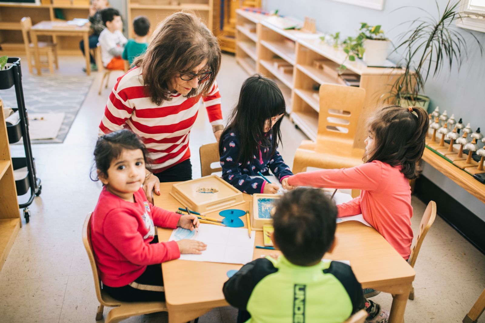 A group of children are sitting at a table in a classroom with a teacher.