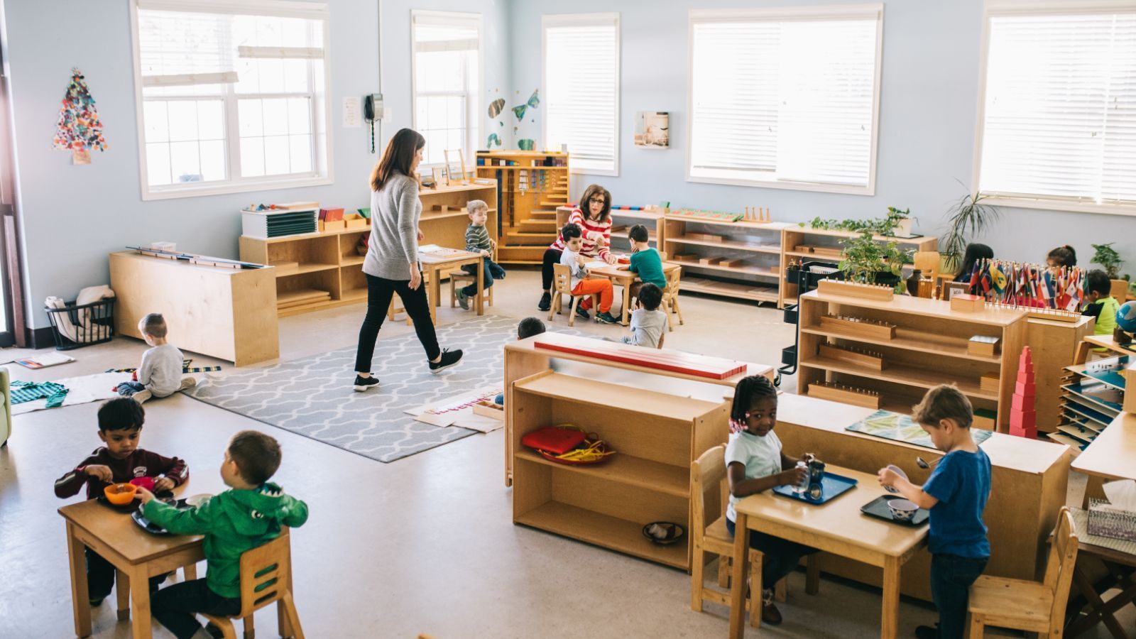 A group of children are sitting at tables in a classroom with a teacher.