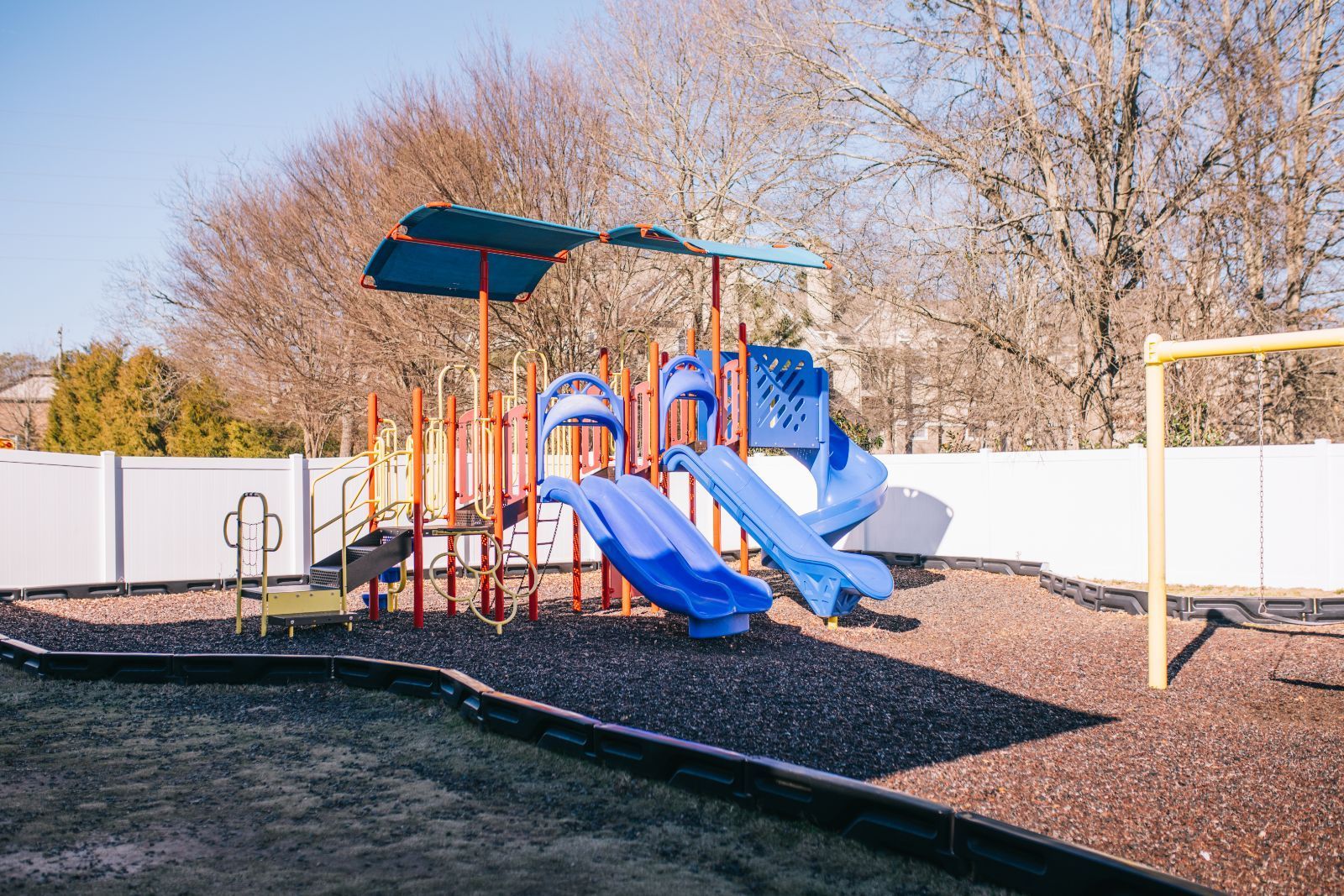 A playground with a slide , swings , and umbrella.