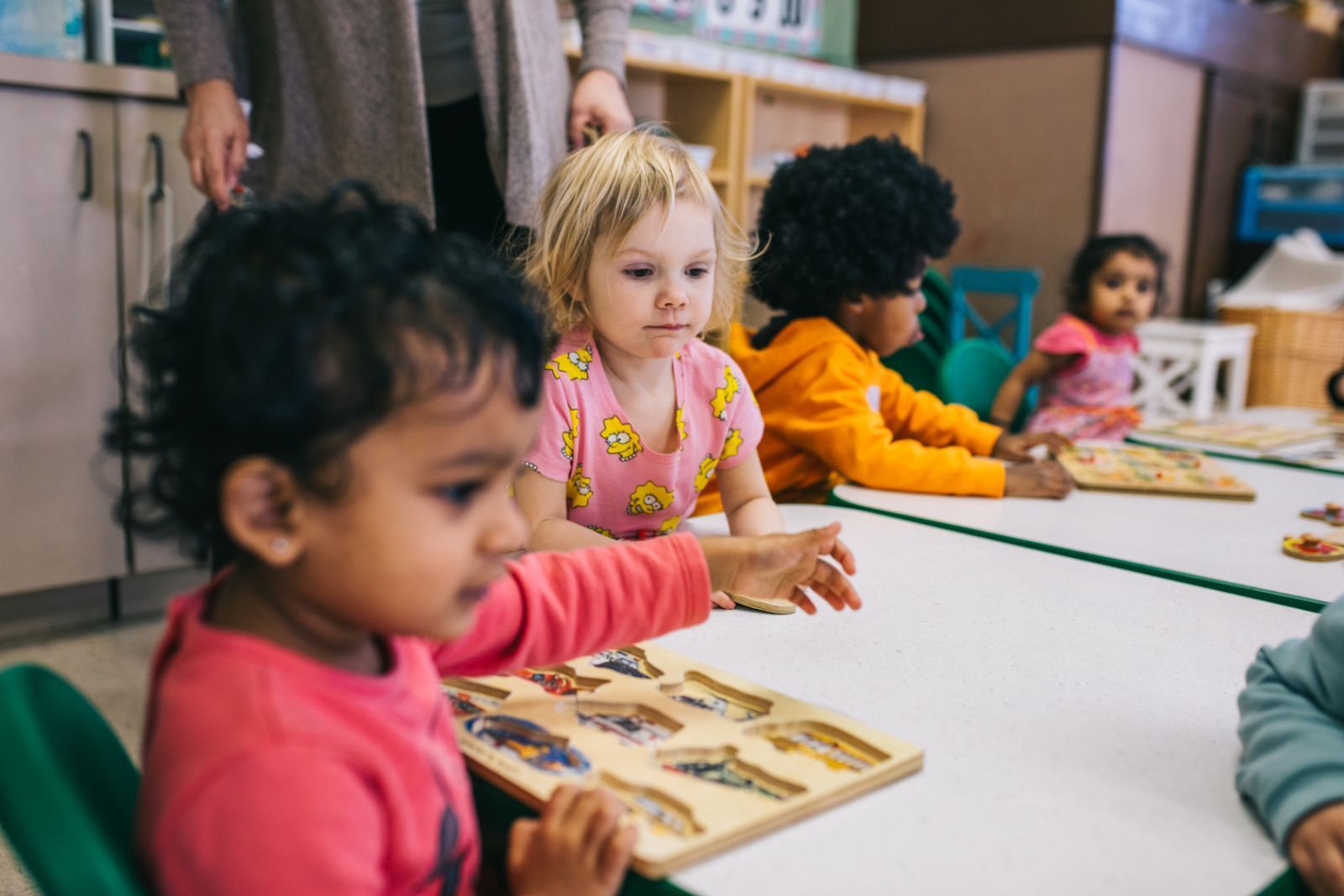 A group of children are sitting at tables in a classroom playing with toys.