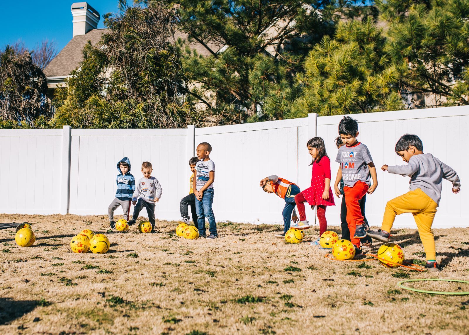 A group of children are playing with soccer balls in a yard.