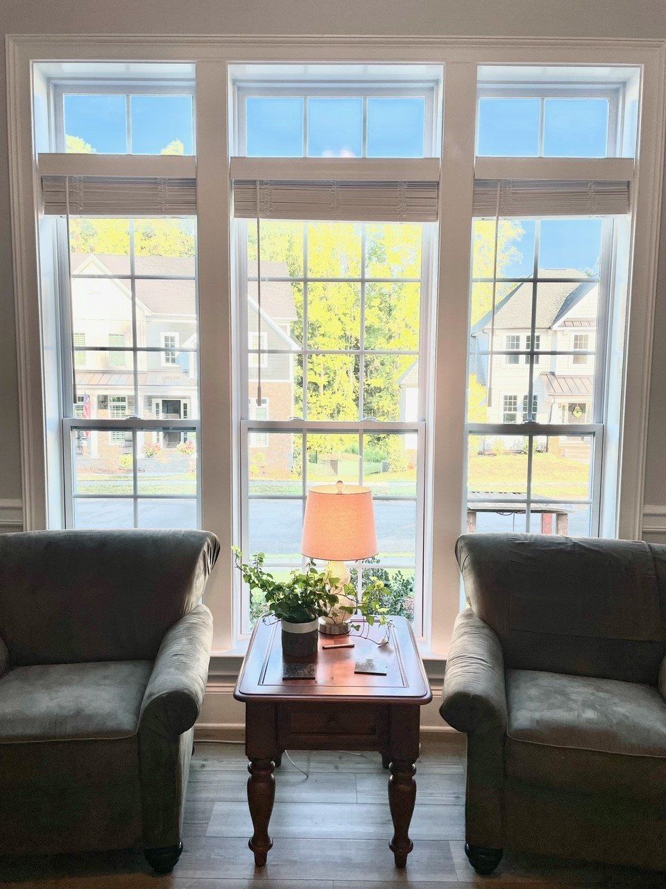 A living room with two chairs and a table in front of three windows.