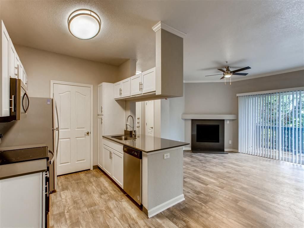 Open-concept kitchen with island and white cabinets; living area with fireplace and sliding glass doors.