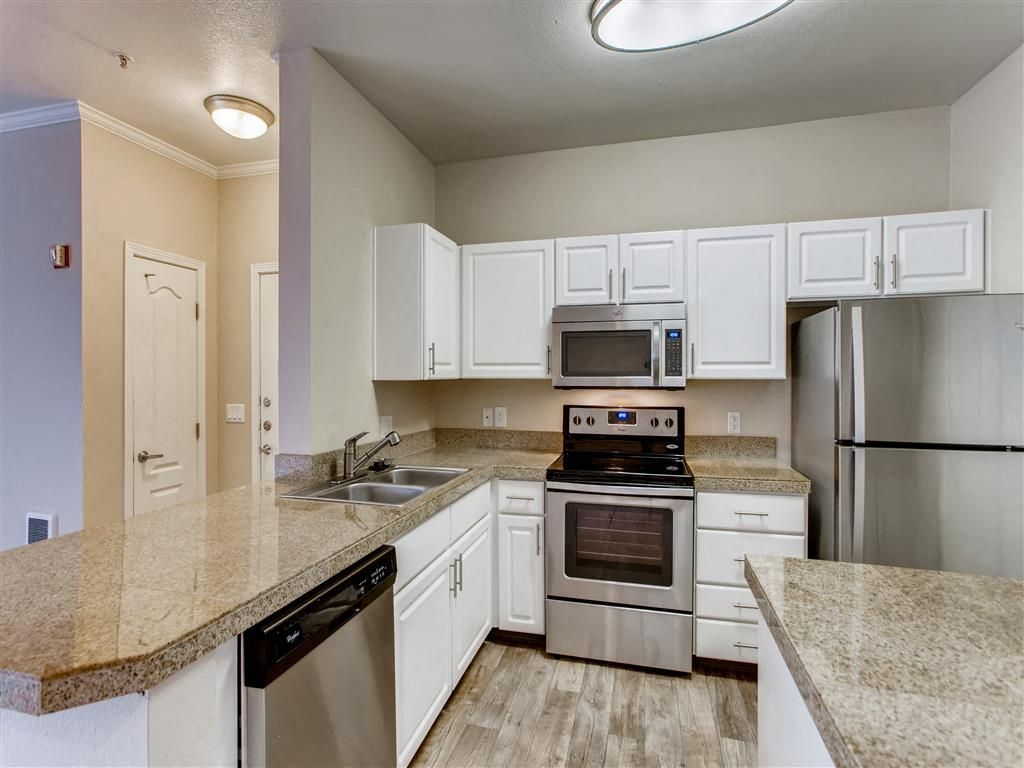 Modern apartment kitchen with white cabinets, granite counters, stainless steel appliances, and a double sink.