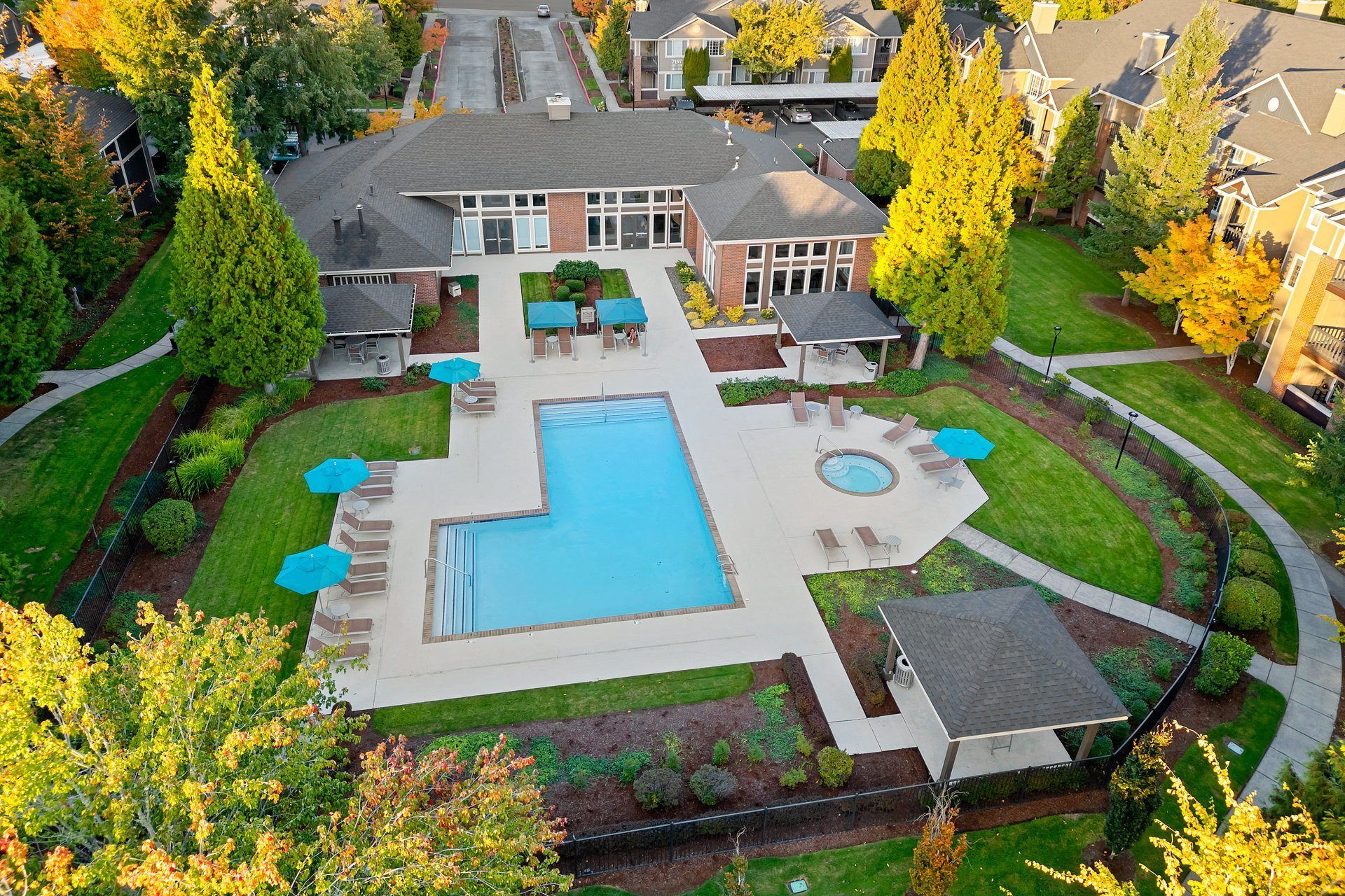 Aerial view of a residential community pool area with lounge chairs and blue umbrellas.