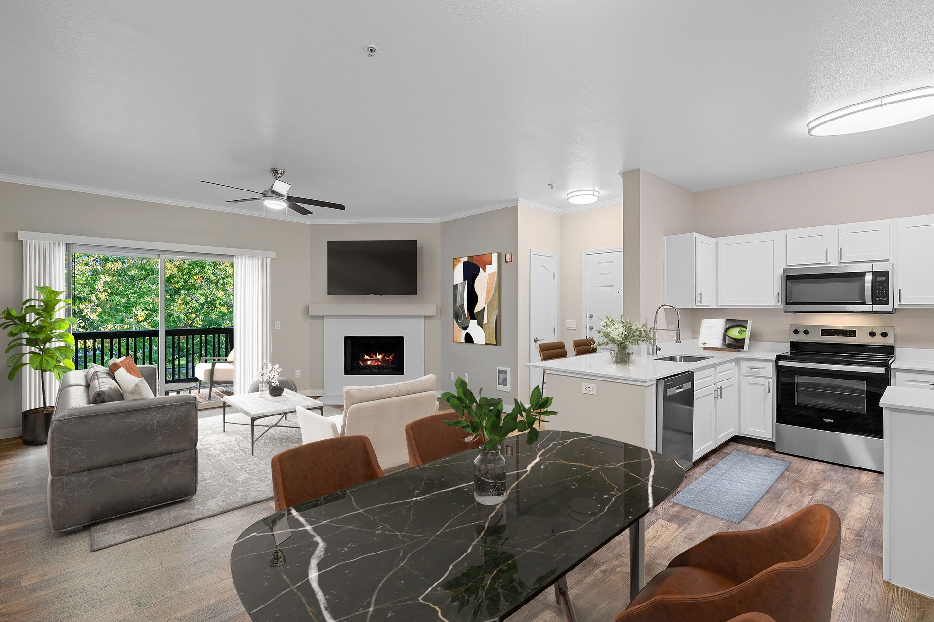 Open-concept living area with a fireplace, TV, and kitchen island opening to a balcony.