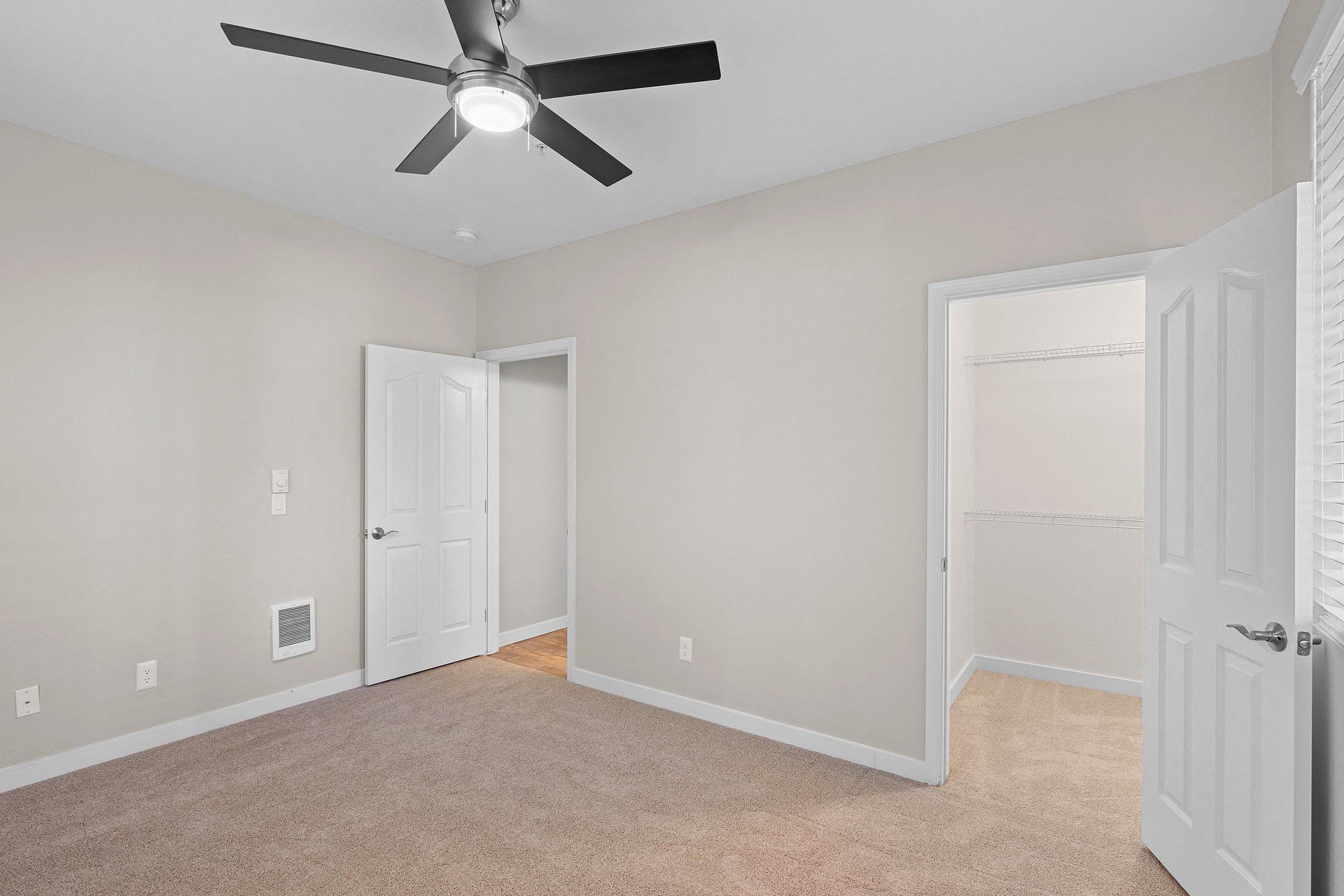 Bedroom interior with beige walls, ceiling fan, and open closet.